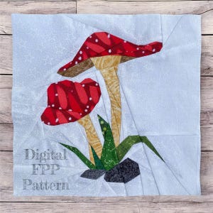 May include: A fabric square with a mushroom design. The mushrooms have red caps with white spots and tan stems. Green leaves and grey rocks are at the base. The text "Digital FPP Pattern" is printed on the fabric.