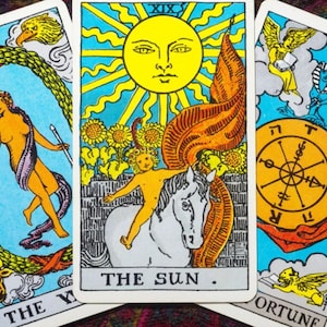 May include: Three tarot cards, The World, The Sun, and Wheel of Fortune. The World card shows a woman dancing in a wreath, The Sun card shows a child riding a white horse, and the Wheel of Fortune card shows a wheel with a sphinx and a bird.