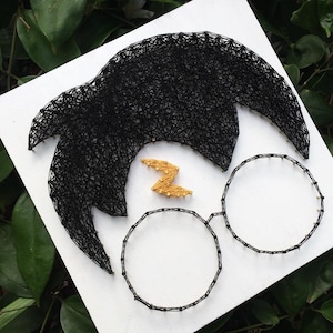 May include: A string art portrait of a character with black hair, round glasses, and a lightning bolt scar. The artwork is created with black thread on a white background, with a gold-colored lightning bolt.