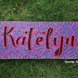 May include: A white ceramic mug with a black handle and the text "But First, Coffee" in a bold, black font. The mug is set against a blurred background. The mug appears to be approximately 10 cm tall.