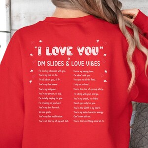 May include: Red sweatshirt with white text that reads "I LOVE YOU" in DM SLIDES & LOVE VIBES. The text includes a list of reasons why someone might love another person.