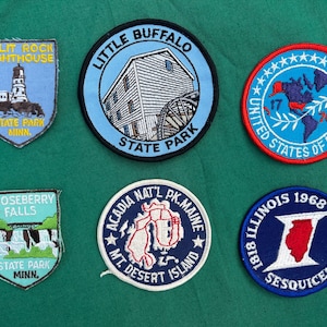 May include: A collection of six embroidered patches featuring various designs. Included are patches for Split Rock Lighthouse, Little Buffalo State Park, and Gooseberry Falls State Park. Other patches commemorate the United States of America and Illinois' Sesquicentennial.