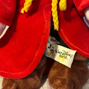 May include: Red plush Mickey Mouse wearing a red robe with yellow trim and a black hat. The plush toy has a "Mickey's" tag and a "Walt Disney World" tag attached to the robe.