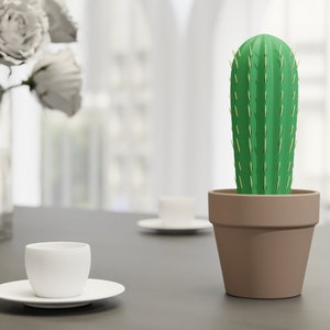 3D-gedruckter Kaktus Zahnstocherhalter in Topffarbe Braun auf einem Tisch neben einer weißen Tasse, imitiert mit herauskommenden Zahnstochern eine Kaktuspflanze.