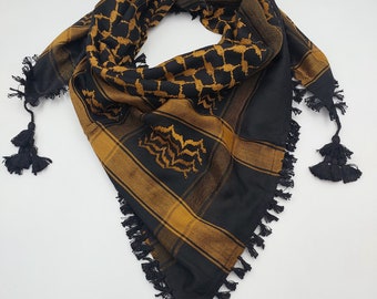 May include: A black and gold patterned headscarf with black tassels. The scarf has a traditional geometric design.