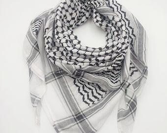 May include: A white and black patterned headscarf with a gray border. The scarf is folded in half and laid flat on a white surface.