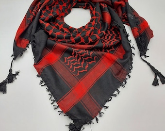 May include: A black and red patterned keffiyeh with black tassels. The keffiyeh is a traditional headscarf worn in the Middle East.