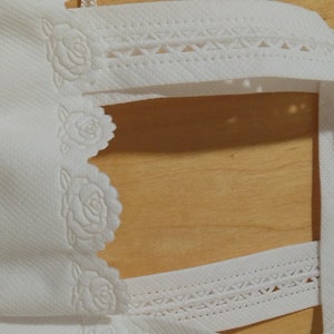 May include: White paper bag with a decorative lace trim and rose pattern. The bag has a handle and is made of a lightweight material.