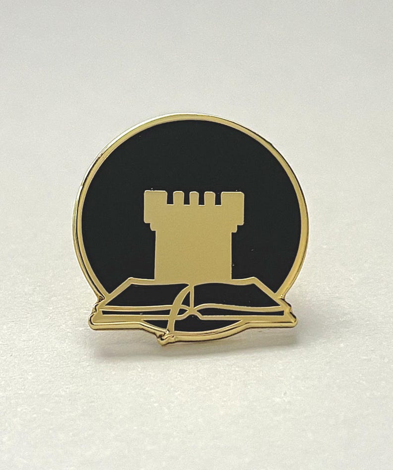 May include: Gold-coloured enamel pin featuring a black circle with a gold tower and a gold open book underneath.