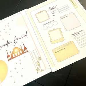 May include: A Ramadan journal with a gold and white design. The cover features a mosque silhouette, stars, and hanging lanterns. The inside pages have sections for "Hello", "About Me", "Favorite Colors", "Favorite Dua", and "Favorite Foods for Iftar".