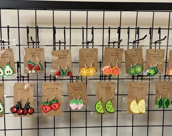 Op de afbeelding: Een collectie pixel art oorbellen in de vorm van diverse vruchten, waaronder watermeloen, aardbei, kers, citroen, limoen en avocado. Elk paar is bevestigd aan een bruine kartonnen displaykaart en verpakt in een doorzichtig plastic zakje.