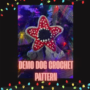 May include: A crocheted Demo Dog pattern in red, white, black, and gray, with the text "Demo Dog Crochet Pattern" and "Created by: Zombie Girl Studio". The image is framed with colorful Christmas lights.