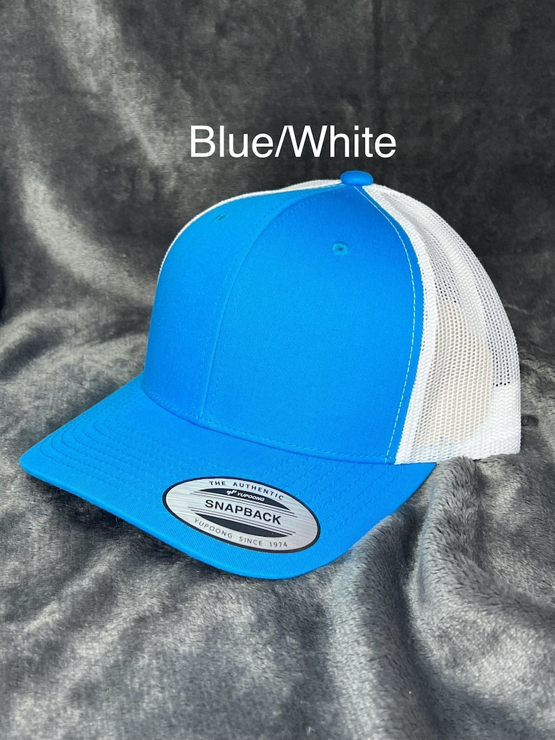 Może przedstawiać: Niebiesko-biała czapka typu snapback z zakrzywionym daszkiem. Przedni panel i daszek są w kolorze jasnoniebieskim, a tył z białej siatki. Czapka ma napis "Blue/White" i etykietę "Snapback".