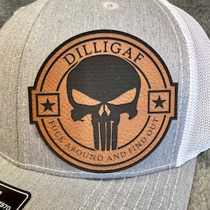 May include: Gray trucker hat with a white mesh back. The front features a brown leather patch with a black skull design and the text "DILLIGAF FUCK AROUND AND FIND OUT".