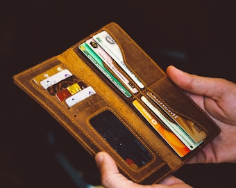 May include: Open, brown leather wallet with multiple card slots filled with various credit cards and identification cards. The wallet is held open, showcasing its interior design and the items stored within. The leather has a distressed appearance.