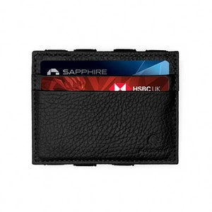 May include: Black leather card holder with two credit cards visible. One card is labeled "SAPPHIRE" and the other "HSBC UK". The card holder has a textured surface and a minimalist design, suitable for carrying essential cards.