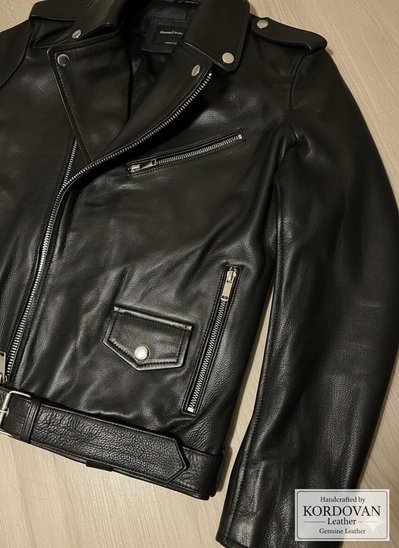 May include: A black leather jacket with a classic biker style. Features include a notched lapel, asymmetrical zipper closure, multiple zippered pockets, and a belted waist. The jacket is made of genuine leather.