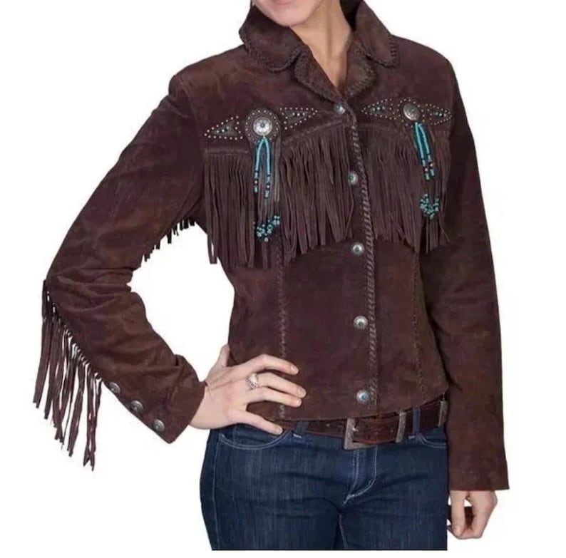 May include: A brown suede jacket with fringe detailing on the chest, sleeves, and back. The jacket features silver-tone buttons and decorative embellishments. The jacket is a western-style garment.