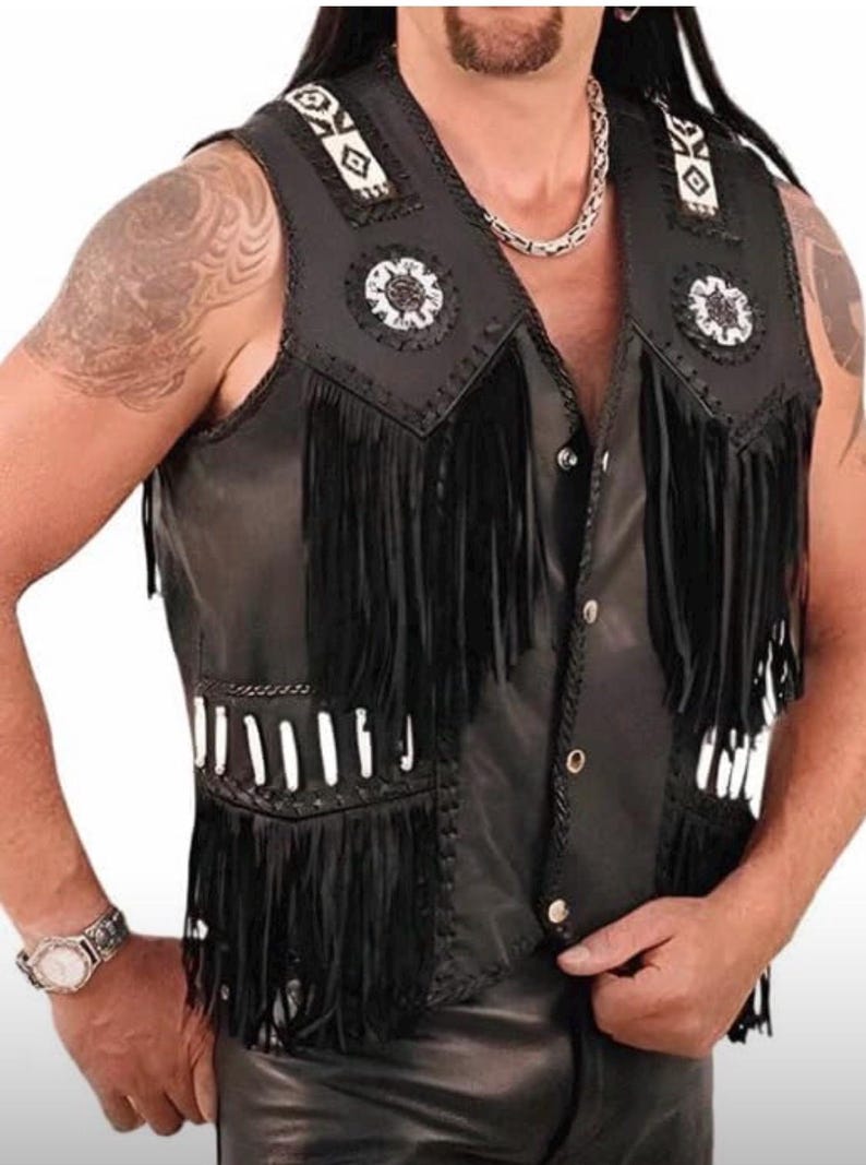 May include: Black leather vest with fringe detailing. The vest features decorative white and black accents on the shoulders and chest, along with white beadwork. The vest has a button-up front and a classic biker style.