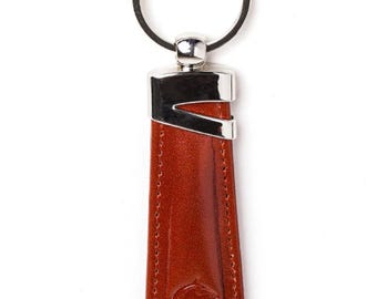 May include: A brown leather keychain with a silver-colored metal accent and key ring. The keychain has a stitched border and a horse head logo at the bottom. The leather is a reddish-brown color.