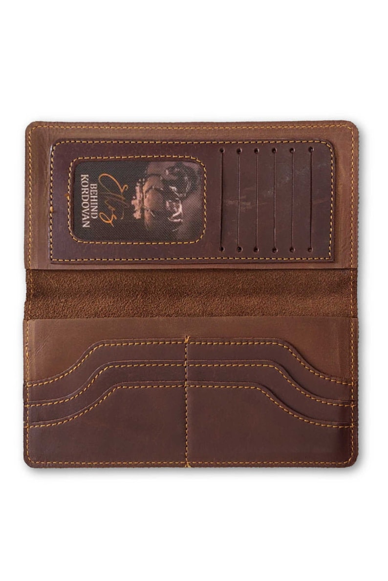 May include: Open brown leather wallet with multiple card slots and bill compartments. The wallet features a clear ID window and is stitched with a contrasting thread. The text "BEHIND KORDOVAN" is visible on the ID window.