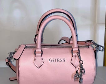 Bolso bandolera Guess rosa con forma de barril y adornos.