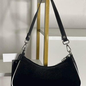 以下が含まれることがあります： 黒い持ち手と「But First, Coffee」のテキストが黒い太字で書かれた白いセラミックマグ。マグは白い表面に置かれています。マグの高さは約10cmです。