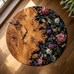 May include: A round table featuring a natural wood slab with a prominent grain pattern on one side and a dark resin section on the other. The resin portion is embedded with various dried flowers, including pink peonies, purple tulips, and small white blossoms.