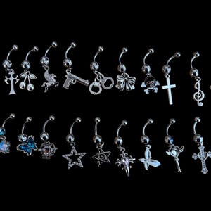 Könnte beinhalten: Eine Auswahl an silberfarbenen Bauchnabelpiercings mit verschiedenen Anhängern, darunter ein Motorrad, ein Kreuz, Kirschen, ein Pegasus, eine Pistole, Handschellen, eine Schleife, ein Totenkopf, ein Notenschlüssel und ein Stern. Einige haben blaue oder rosa Akzente. Schwarzer Hintergrund.