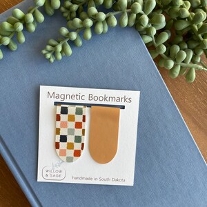 May include: Two magnetic bookmarks. One bookmark is orange and the other is a colorful plaid pattern. The bookmarks are on a white card with the text "Magnetic Bookmarks", "Willow & Sage", and "handmade in South Dakota".