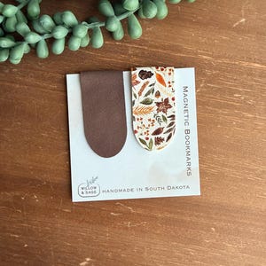May include: Two magnetic bookmarks attached to a white display card. One bookmark is solid brown, and the other features a white background with a colorful autumn leaf and acorn pattern. The card reads Magnetic Bookmarks and Willow & Sage Handmade in South Dakota.
