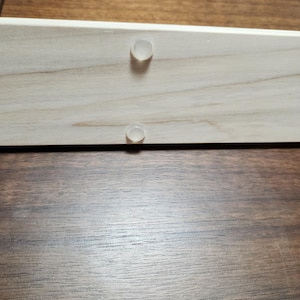 May include: Two clear plastic bumpers are attached to a light wood surface. The wood surface is likely part of a piece of furniture.