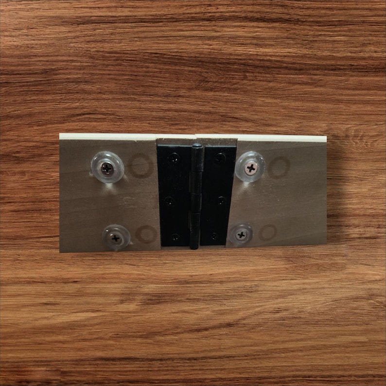 May include: A black metal hinge with four clear plastic screw covers. The hinge is attached to a silver metal plate.