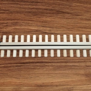 May include: A wooden loom with a black strap, featuring 20 dowels for weaving.