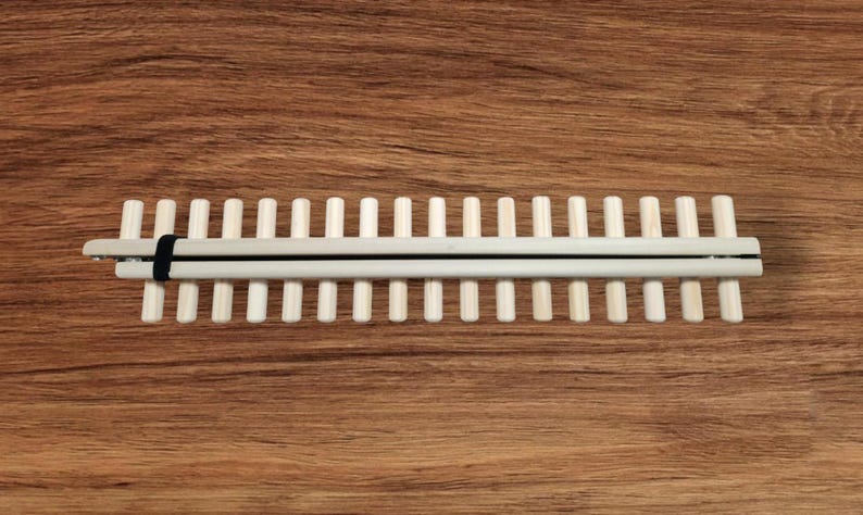 May include: A wooden loom with a black strap, featuring 20 dowels for weaving.