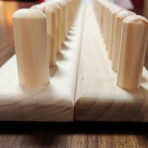 May include: A wooden peg board with rows of wooden pegs. The board is made of light wood and the pegs are a slightly darker shade of wood.