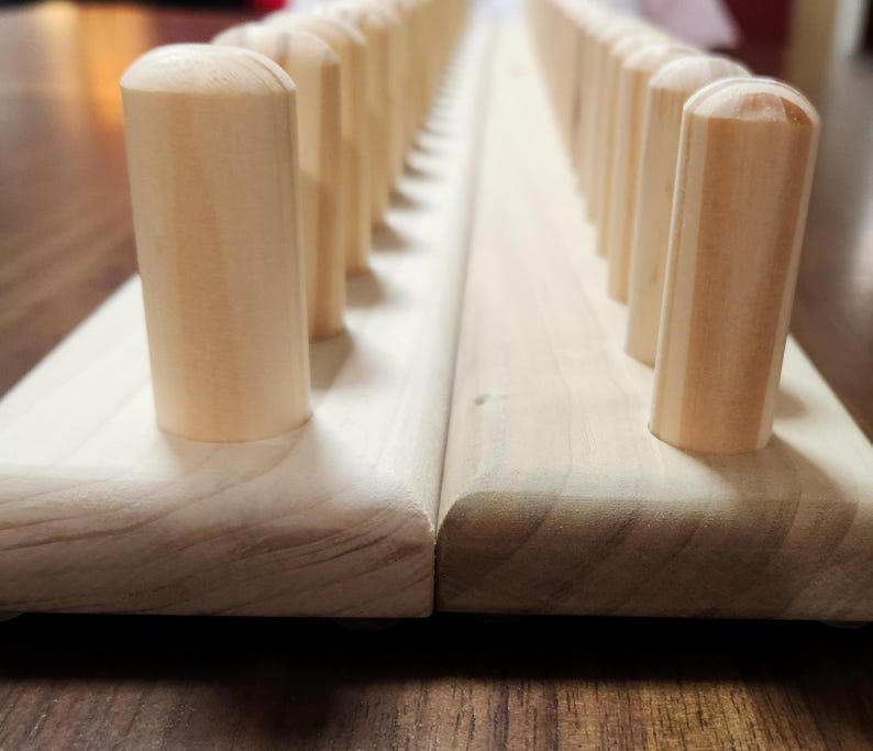May include: A wooden peg board with rows of wooden pegs. The board is made of light wood and the pegs are a slightly darker shade of wood.