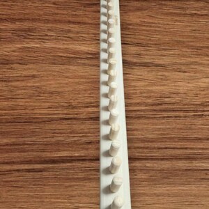 May include: A wooden knitting loom with 40 pegs. The loom is white and the pegs are natural wood.