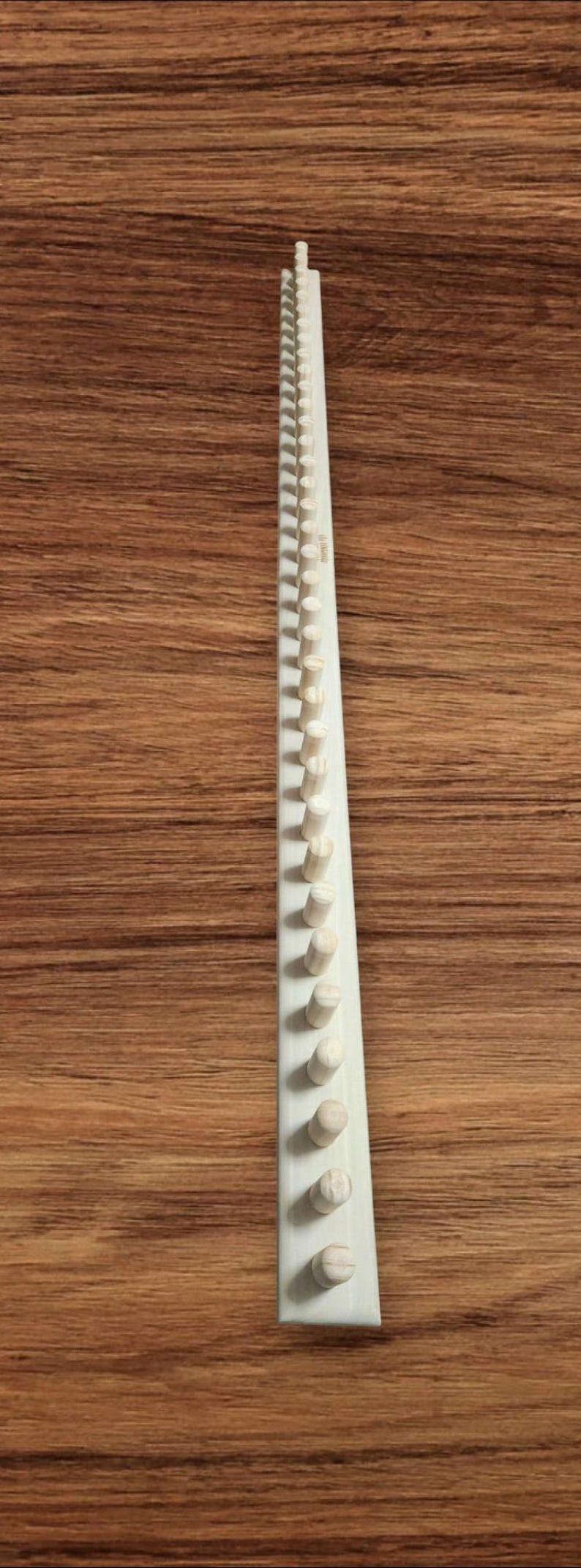 May include: A wooden knitting loom with 40 pegs. The loom is white and the pegs are natural wood.