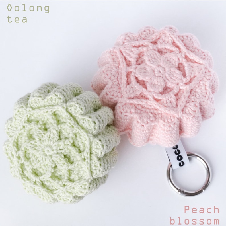 Pu&ograve; includere: Due portachiavi all'uncinetto, uno verde e uno rosa, con il testo "Oolong tea" e "Peach blossom" su uno sfondo bianco.
