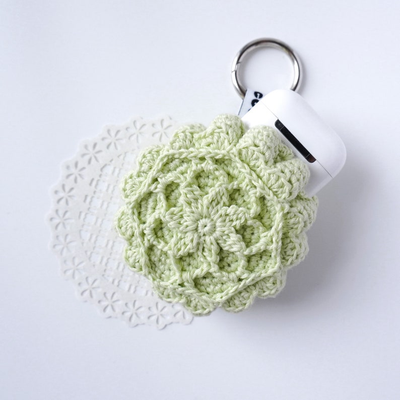 Pu&ograve; includere: Una custodia in crochet verde chiaro per un paio di auricolari wireless con un portachiavi argentato.