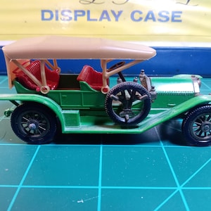 May include: A green toy car with a tan roof and red seats. The car has a spare tire on the back and four wheels.