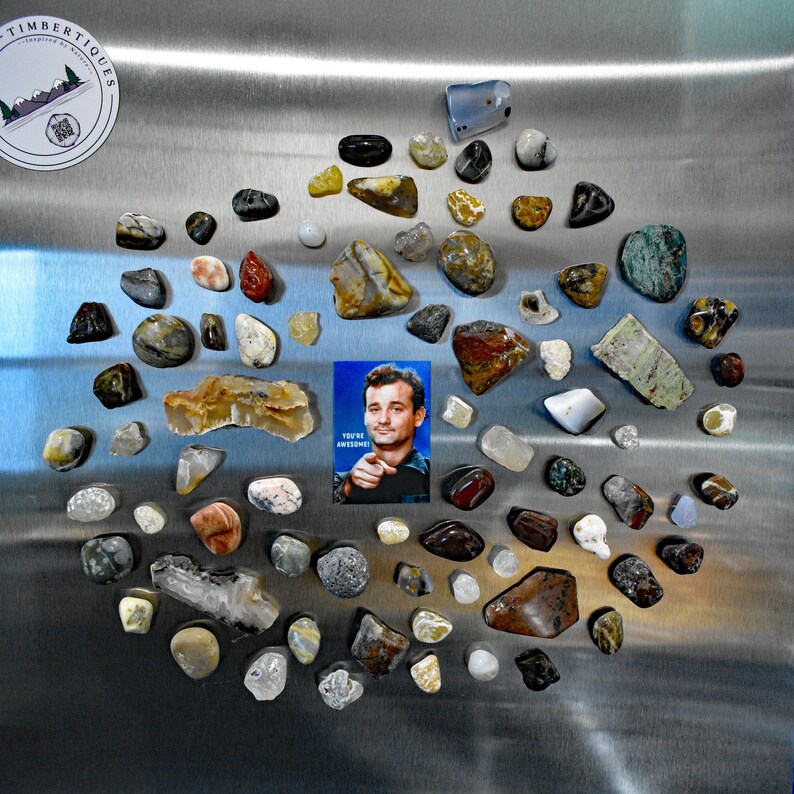May include: A collection of polished rocks and stones in various shapes, sizes, and colors, including brown, gray, white, and red. A small card with the text "YOU'RE AWESOME!" and a picture of Bill Murray is also included.