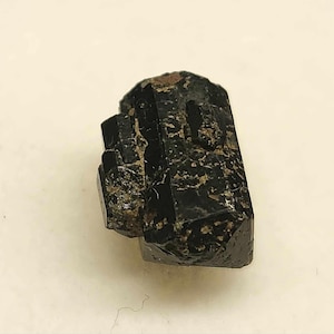 May include: A black, faceted, crystal with a pointed tip. The crystal has a rough, textured surface.