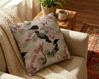Può includere: Un cuscino quadrato con un motivo intrecciato di strolaghe nere e bianche intervallate da motivi floreali rosa e verdi su uno sfondo beige chiaro. Il tessuto ha un aspetto strutturato con dettagli del filo visibili in tutto il design.