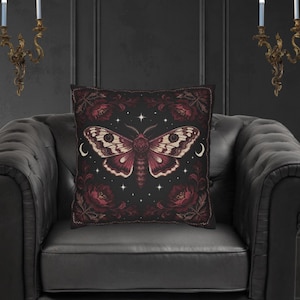 Può includere: Cuscino decorativo nero con un motivo a falena bordeaux e crema. La falena è al centro, circondata da motivi floreali e stellati. Il cuscino è quadrato e poggia su una poltrona in pelle nera. Misura circa 40 cm x 40 cm.