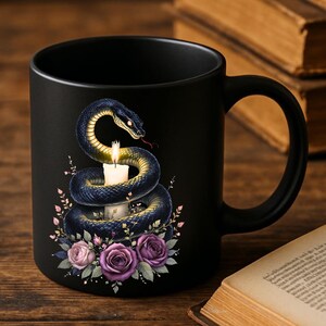 Puede incluir: Taza de cerámica negra con un diseño de una serpiente azul y dorada enrollada alrededor de una vela encendida. La serpiente está rodeada de rosas rosas y moradas y hojas verdes. La taza tiene un asa curva.