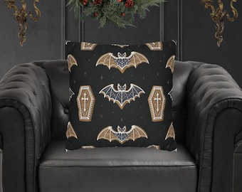 May include: A black decorative throw pillow with a repeating pattern of bats and coffins. The bats are brown with blue accents, and the coffins have a cross design. The pillow is on a black leather chair.