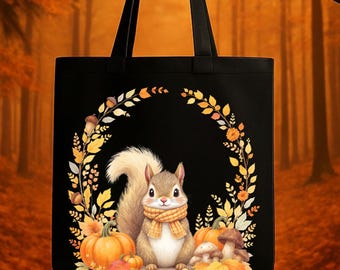May include: Black tote bag featuring a squirrel wearing a scarf, surrounded by pumpkins, mushrooms, and fall foliage. The design is set against a black background, with a wreath of leaves and acorns. The bag has two black handles.