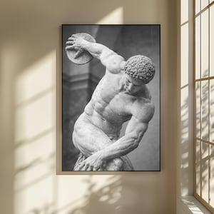 Könnte beinhalten: Schwarz-Weiß-Druck in einem Rahmen einer klassischen Skulptur, die eine muskulöse Figur beim Diskuswerfen zeigt. Die Skulptur ist detailliert und zeigt den Körperbau des Mannes und die Scheibe in seiner Hand. Das Kunstwerk wird an einer Wand ausgestellt.